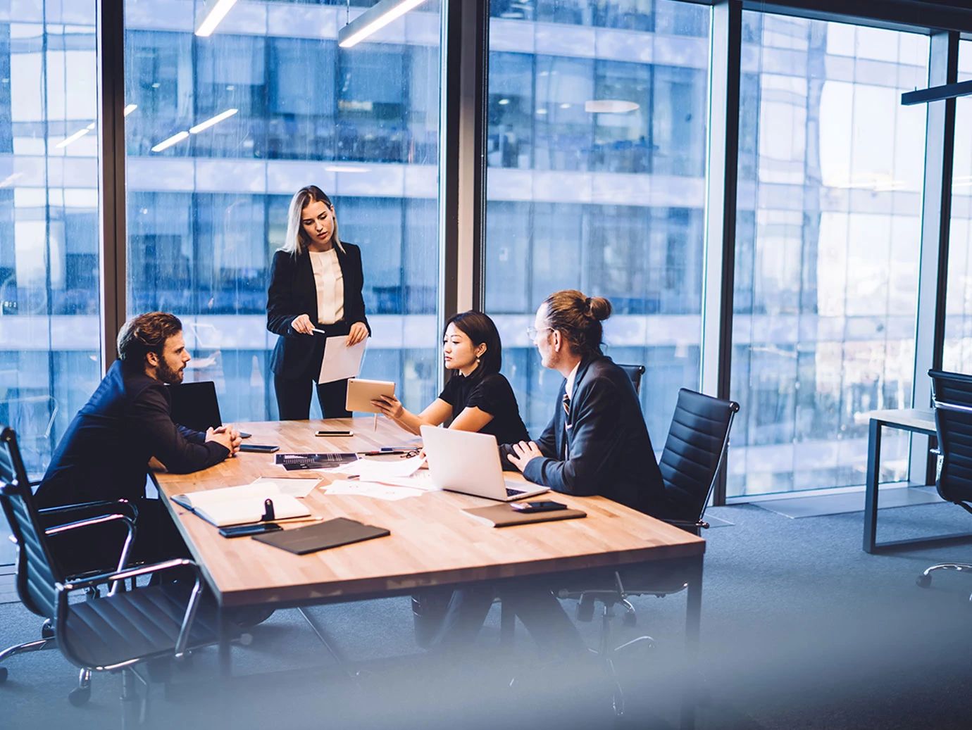 Business team meeting in a modern conference room with large glass windows.